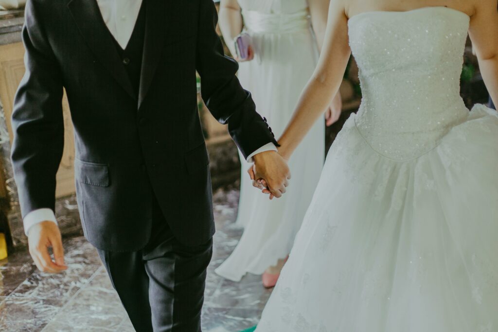 pexels-photo-1043902-1043902 A romantic moment capturing a bride and groom holding hands in elegant wedding attire indoors.