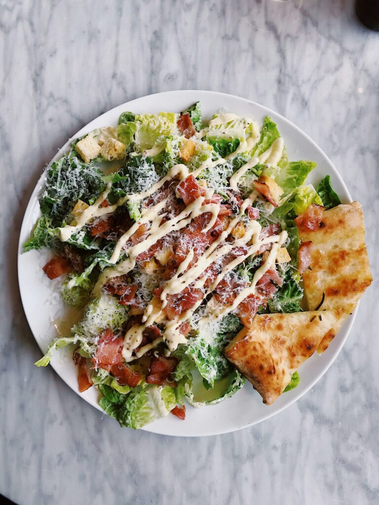 pexels-photo-2097090-2097090 Tasty Caesar salad topped with bacon, cheese, and drizzled sauce, served with crispy bread.